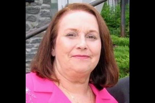 Lyn Simon, a woman with shoulder-length auburn hair, wearing a pink lapeled jacket, smiles at the camera.